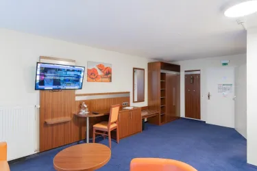 Ein komfortables Zimmer mit einem Tisch, Stühlen und einem Fernseher an der Wand. Die Einrichtung ist modern und in warmen Farben gehalten.