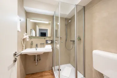 Ein modernes Badezimmer mit einer gläsernen Dusche und einem Waschbecken. Die Wände sind in neutralen Farbtönen gehalten, und der Boden ist aus Holz.