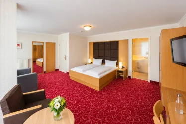 Ein komfortables Hotelzimmer mit einem Doppelbett und modernem Mobiliar. Die warme Farbgestaltung und der gemütliche Sitzbereich schaffen eine einladende Atmosphäre.