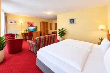 Ein gemütliches Hotelzimmer mit einem Doppelbett und einer komfortablen Sitzecke. Die Wände sind in warmen Tönen gehalten, und es gibt Pflanzen für eine einladende Atmosphäre.