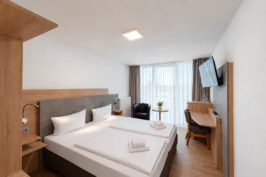 Ein modernes Hotelzimmer mit zwei Einzelbetten und stilvollen Möbeln. Große Fenster sorgen für viel Tageslicht und eine angenehme Atmosphäre.