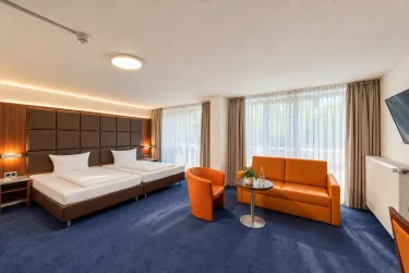 Ein modernes Zimmer mit zwei Einzelbetten und einem komfortablen Wohnbereich. Große Fenster sorgen für viel Tageslicht und eine einladende Atmosphäre.