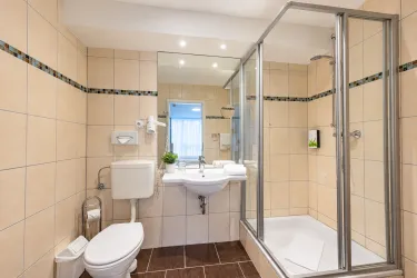 Ein modernes Badezimmer mit beige gefliesten Wänden und einer Glasdusche. Es ist gut beleuchtet und enthält eine Toilette sowie ein Waschbecken mit Spiegel.
