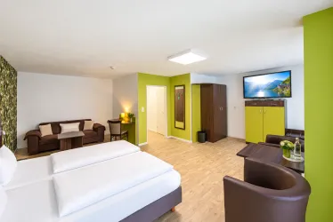 Ein helles Zimmer mit zwei Einzelbetten und modernen Möbeln. Die Wände sind in freundlichen Farben gestrichen und es gibt einen Fernseher sowie eine Sitzecke.