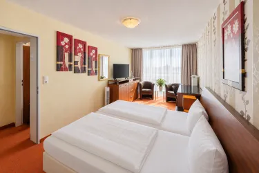 Ein modernes Hotelzimmer mit zwei Einzelbetten und einem gemütlichen Sitzbereich. Große Fenster lassen viel Tageslicht herein und schaffen eine einladende Atmosphäre.