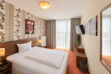 Ein modernes Hotelzimmer mit einem Doppelbett und stimmungsvollem Licht. Große Fenster sorgen für viel Tageslicht und eine angenehme Atmosphäre.