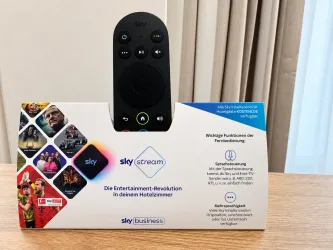 Ein Sky Stream Gerät mit Fernbedienung, das auf einem Tisch steht. Es bietet verschiedene Funktionen für das Entertainment im Hotelzimmer.