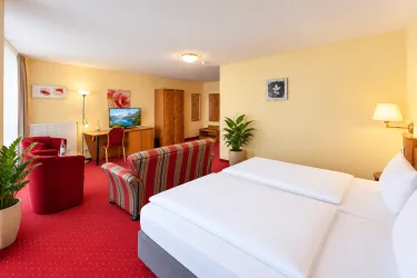 Ein gemütliches Hotelzimmer mit einem großen Doppelbett und stilvoller Einrichtung. Im Raum befinden sich ein Fernseher und ein komfortabler Sitzbereich.