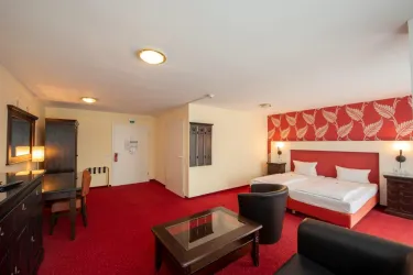 Ein helles Hotelzimmer mit rotem Teppich, zwei Betten und einer Sitzgelegenheit. Die Wände sind teilweise mit einem blühenden Muster dekoriert.