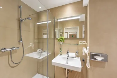Ein modernes Badezimmer mit einer Glasdusche und einem eleganten Waschbecken. Die Wände sind in einem warmen Beige-Ton gehalten, und eine kleine Pflanze sorgt für einen frischen Akzent.