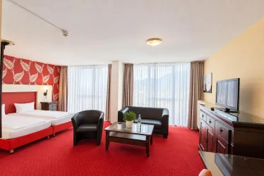 Ein modernes Hotelzimmer mit rotem Teppich und stilvoller Einrichtung. Es gibt ein Doppelbett, eine Sitzecke und große Fenster mit Blick auf die Landschaft.