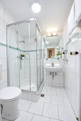 Ein modernes Badezimmer mit einer Duschkabine und weißen Fliesen. Der Raum ist hell und bietet grundlegende Sanitäranlagen.