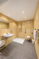 Ein modernes Badezimmer mit beigen Fliesen und einer Dusche. Es gibt eine Toilette und einen Waschplatz mit Spiegel.