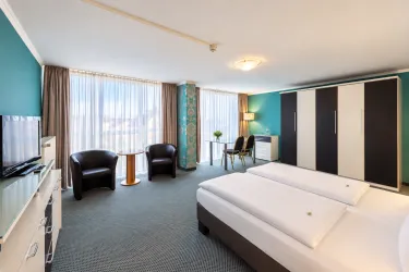 Ein helles Hotelzimmer mit zwei Einzelbetten und modernen Möbeln. Große Fenster sorgen für viel Tageslicht und eine einladende Atmosphäre.