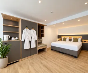 Ein modernes Hotelzimmer mit zwei Betten und einem gemütlichen Sitzbereich. Die Einrichtung umfasst einen Kleiderschrank, Bademäntel und Pflanzen für eine einladende Atmosphäre.