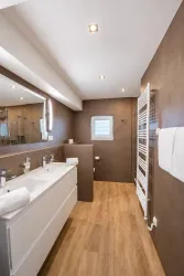 Ein modernes Badezimmer mit braunen Wänden und einem hellen Boden. Es gibt ein Waschbecken, einen Handtuchhalter und ein Fenster.