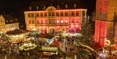 Ein festlicher Marktplatz bei Nacht mit vielen Besuchern. An den Ständen gibt es festliche Lichter und eine schön dekorierte Umgebung.
