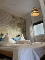 Ein gemütliches Schlafzimmer mit einem großen Bett und dekorativen Kopfkissen. Die Wand hat einen rustikalen Look und eine stilvolle Lampe hängt von der Decke.