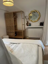 Ein modernes Schlafzimmer mit einem Bett und einem Holzkasten zur Aufbewahrung. An der Wand hängt ein runder Spiegel und eine Lampe sorgt für angenehmes Licht.