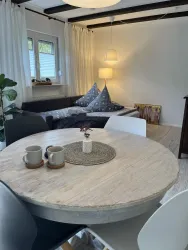 Ein gemütlicher Wohnbereich mit einem runden Tisch und zwei Tassen. Im Hintergrund sind ein Sofa und eine Stehlampe zu sehen.