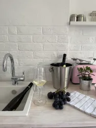 Eine elegante Küche mit einem Flasche Sekt in einem Eiskübel. Neben dem Kübel stehen Gläser und frische Trauben auf einem Tisch.