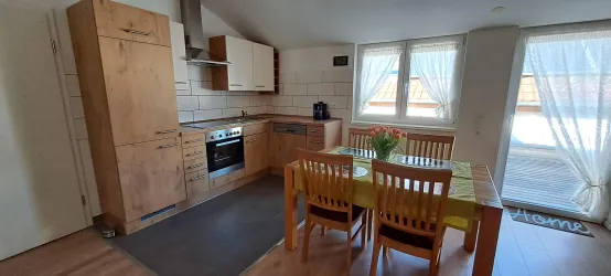 Eine moderne Küche mit Holzschränken, einem Esstisch für vier Personen und großen Fenstern. Das natürliche Licht macht den Raum hell und einladend.