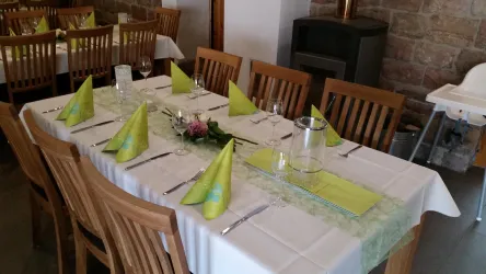 Ein festlich gedeckter Tisch mit grünen Servietten und Blumenarrangement. Die Holzstühle und der Kamin im Hintergrund verleihen eine gemütliche Atmosphäre.