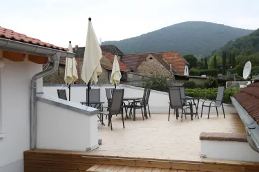 Eine Terrasse mit Tischen und Stühlen, mit Blick zum Schloßberg. Es gibt Sonnenschirme, die Schatten spenden.