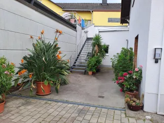 Ein kleiner Innenhof mit blühenden Pflanzen in Töpfen. Treppe im Hintergrund führt in die 1. Etage, wo sich der Zugang zu unseren Ferienwohnungen befindet.
