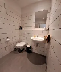 Ein modernes Badezimmer mit weißen Fliesen und grauem Boden. Es enthält ein Waschbecken, eine Toilette und einen Spiegel.