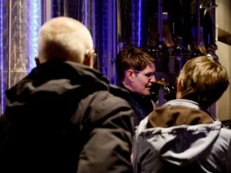 Eine Person erklärt etwas in einer Brauerei. Im Hintergrund sind interessierte Zuhörer zu sehen.