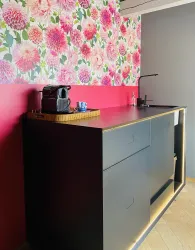 Eine moderne Küchenecke mit einer schwarzen Arbeitsfläche und einem bunten Blumenmuster hinter der Wand. Auf der Arbeitsfläche stehen eine Kaffeekanne und eine Tasse.