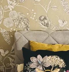 Ein stilvolles Kopfteil mit einer grauen Polsterung und dekorativen Kissen. Im Hintergrund ist eine Blumenmotivan Wandtapete zu sehen.