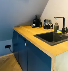 Eine moderne Küchenzeile mit einem Holzarbeitsplatz und einer dunklen Spüle. Auf der Arbeitsfläche stehen Gläser und eine Kaffeemaschine.