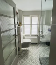 Ein modernes Badezimmer mit einer großen Dusche und einem weißen WC. Die Wände sind hell und der Boden hat ein dekoratives Muster.