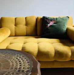 Ein gelbes Sofa mit einer glatten Oberfläche und einer dekorativen Kissen. Neben dem Sofa steht ein runder Tisch mit einem filigranen Design.