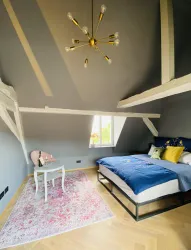 Ein elegantes Schlafzimmer mit einem großen Bett und einem modernen Kronleuchter. Der Raum hat eine helle Atmosphäre und ist mit einem schönen Teppich dekoriert.