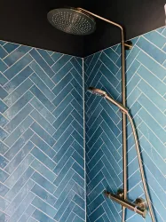 Eine moderne Dusche in einer Ecke mit blauen, schräg verlegten Fliesen. Der Duschkopf ist elegant und aus Metall.