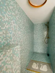 Ein modernes Badezimmer mit azurblauen Fliesen und einer eleganten Duschkabine. Auf dem Boden liegt ein grauer Teppich mit einem Schwan-Design.