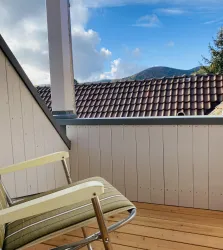 Ein gemütlicher Balkon mit einem Stuhl und Blick auf die Berge. Die Wolken am blauen Himmel verleihen der Szene eine entspannte Atmosphäre.