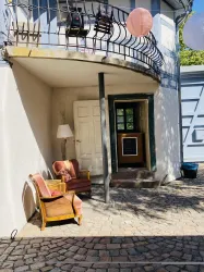 Ein einladender Eingangsbereich mit einem Balkon und einem gepflasterten Boden. Es gibt zwei Stühle und eine Lampe, die eine gemütliche Atmosphäre schaffen.