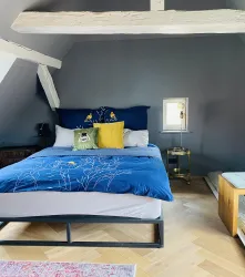 Ein gemütliches Schlafzimmer mit einem modernen Bett und blauer Bettwäsche. Die Wände sind in einem dunklen Grauton gestrichen und Holzdetails verleihen dem Raum eine einladende Atmosphäre.