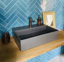 Ein elegantes Waschbecken auf einem Holzregal. Der Hintergrund besteht aus blauen, schräg verlegten Fliesen und einem dekorativen Spiegelrahmen.