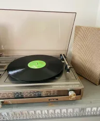 Ein Plattenspieler mit einer Schallplatte und einem grünen Etikett. Daneben steht ein Lautsprecher in einem retro Stil.