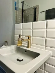 Ein modernes Badezimmer mit einem eleganten Waschbecken und goldenen Armaturen. Die dekorativen Fliesen und das Glasduschabtrennung verleihen dem Raum einen stilvollen Touch.