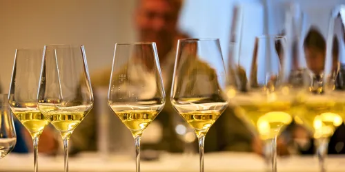 Ein Mensch gieß einen roséfarbenen Wein in mehrere Gläser. Die Gläser stoßen an und reflektieren das Licht.