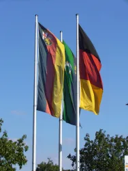 Drei Fahnen wehen im Wind, darunter die deutsche Flagge. Der Himmel ist klar und blau.