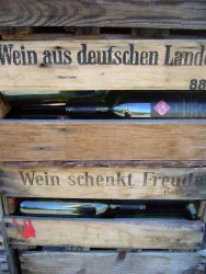 Ein Holzgestell mit Flaschen, die in Kisten stehen. Auf den Kisten steht der Schriftzug "Wein aus deutschen Landen" und "Wein schenkt Freude".