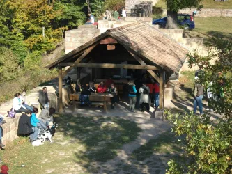 Eine gemütliche Hütte im Freien mit vielen Menschen, die sich versammeln. Umgeben von Bäumen und natürlicher Landschaft.