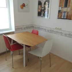 Ein kleiner Essbereich mit einem Holztisch und vier Stühlen. Zwei Stühle sind rot und zwei sind weiß.